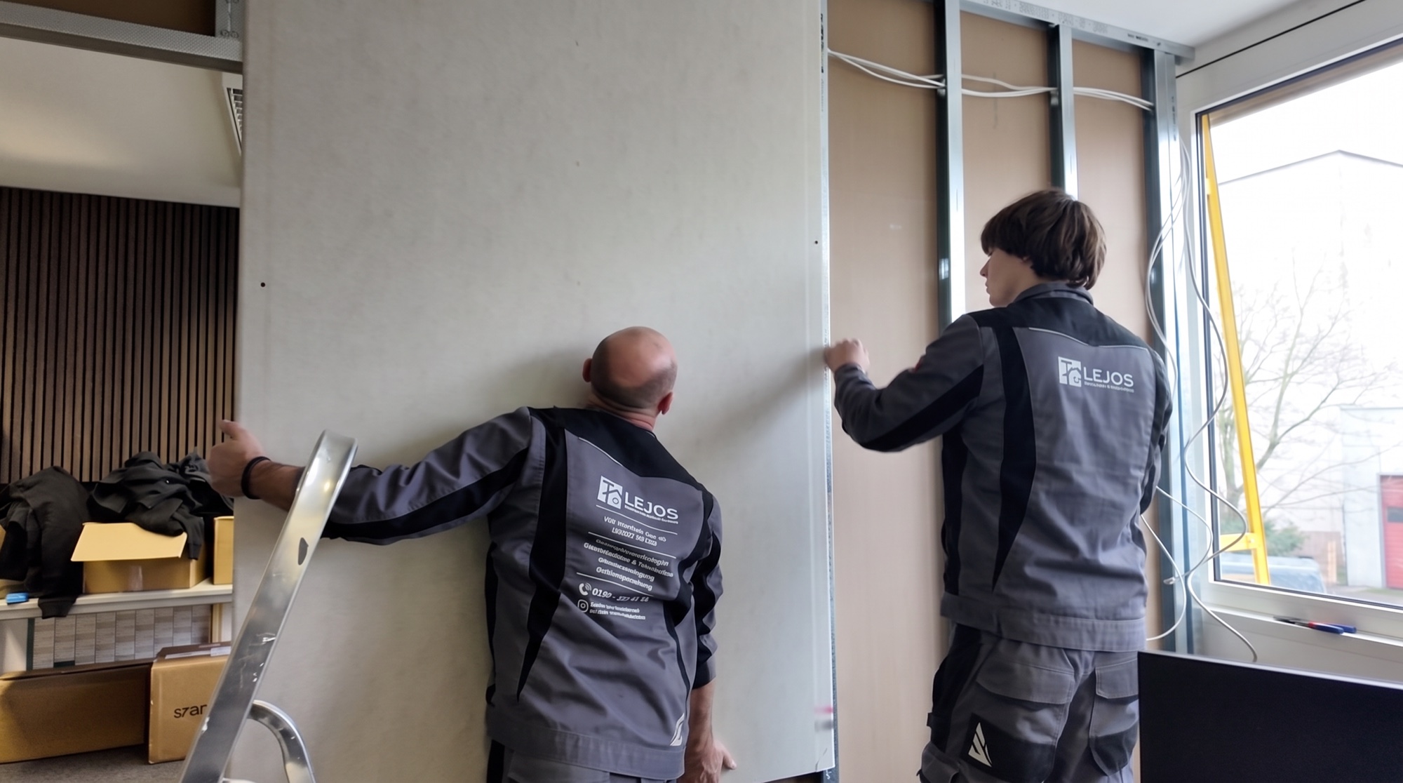 Zwei Monteure setzen eine große Gipsplatte an das Ständerwerk
